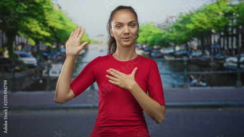 Konstfotografi Woman with raised right hand and left hand on chest on street making oath pledge gesture in front of canal and bridge; sincerity apology