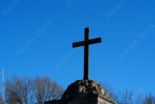 Black stone cross monument against a clear blue sky background