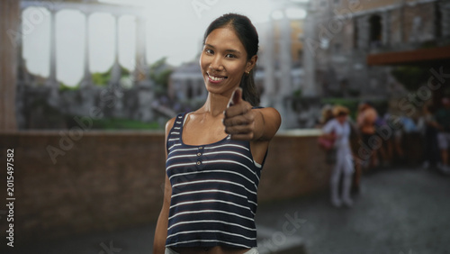 Fotografie Thai woman showing thumbsup with a closed eye smile in a historic building plaza; confidence travel journey