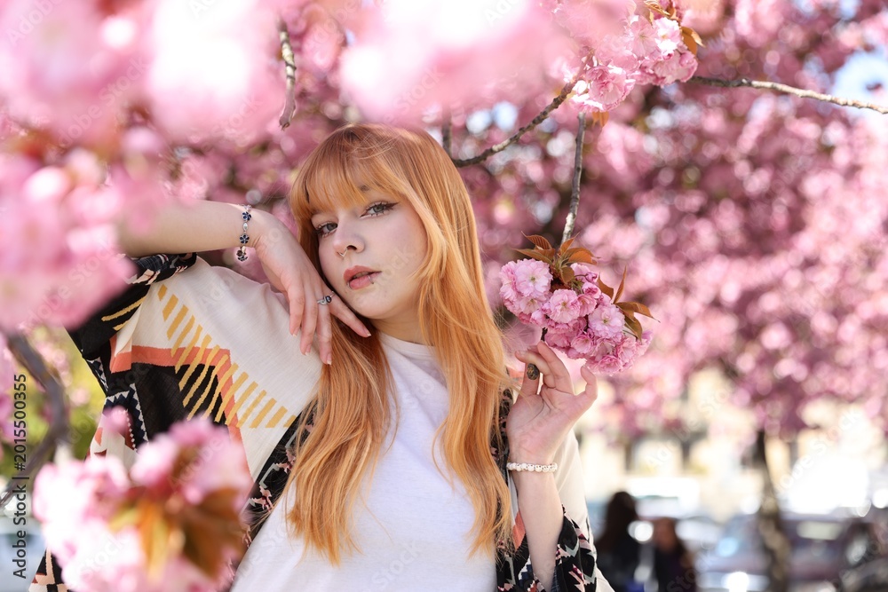Fototapeta premium Beautiful young girl posing near blossoming sakura tree outdoors. Space for text