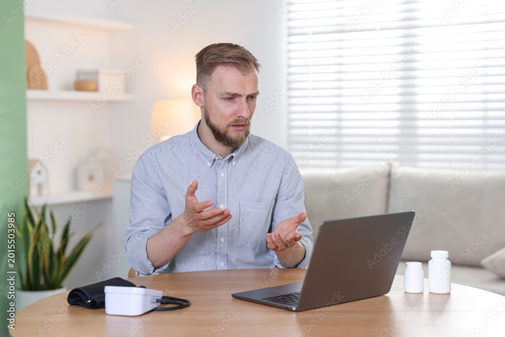 Fototapeta premium Telemedicine. Man having online consultation with doctor via laptop at wooden table indoors