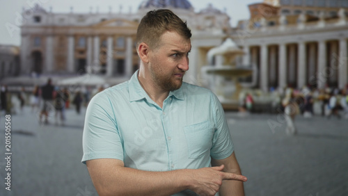 Photos Man pointing finger with right hand near fountain in building square, wearing short sleeve shirt and gesturing toward lower right; skepticism