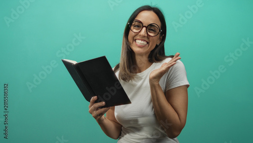 Foto Woman holds black hardcover book, reading aloud while smiling, waving hand and wearing glasses and white tshirt in studio; joyful learning