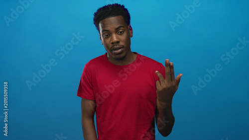Foto Young african american man wearing red shirt pointing finger toward camera in blue studio; confidence