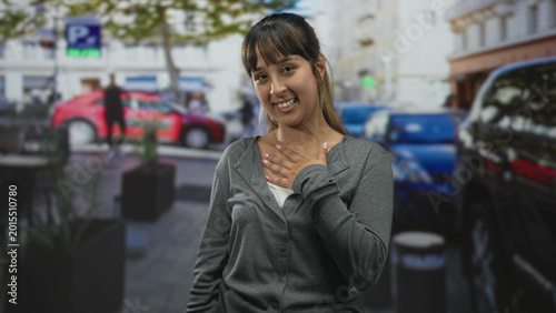 Konstfotografi Woman hand on chest gesture in street with parked cars, planters and building facades; gratitude sincerity