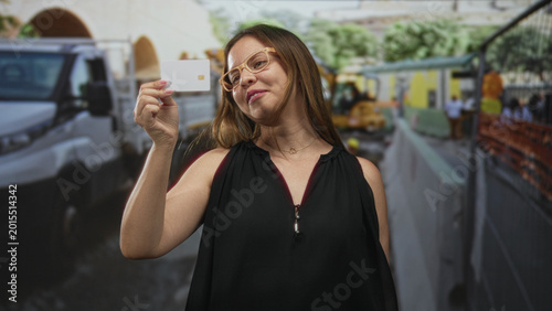 Foto Woman wearing glasses holding creditcard up showing chip at building construction site smiling; confidence verification