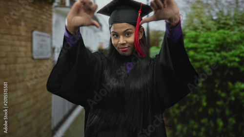 Фотография Woman in graduation cap and gown giving thumbsdown gesture on street near building facade; rejection
