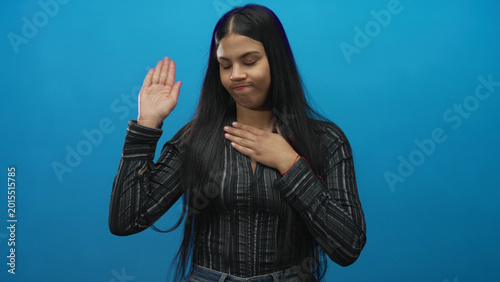 Canvas Print Woman raising hand and placing palm on chest in blue studio; seriousness sincerity promise commitment