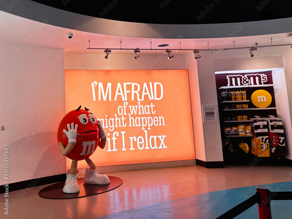 Fototapeta premium Red M and M mascot in a bright shop display with illuminated sign reading I'm afraid of what might happen if I relax at an M and M store in London UK