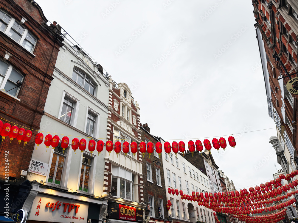 Fototapeta premium Red lanterns and Chinatown street decorations over a London, UK shopping street with historic brick buildings and restaurants celebrating cultural festival