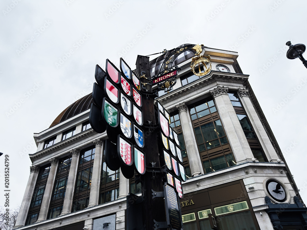 Fototapeta premium Historic building facade with Swiss Court heraldic shields and ornate hanging sign in central London, UK, classical columns clock and dome on a commercial street corner