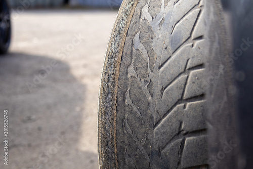 A close view shows a worn out car tire resting on a parking lot surface. The tire surface shows clear signs of wear with little tread remaining
