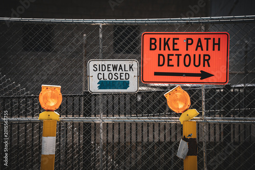 фотографія Construction signs indicate sidewalk closure and bike path detour with flashing