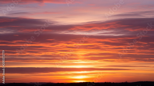 Vászonkép Vibrant orange sunset with scattered clouds in the sky at dusk