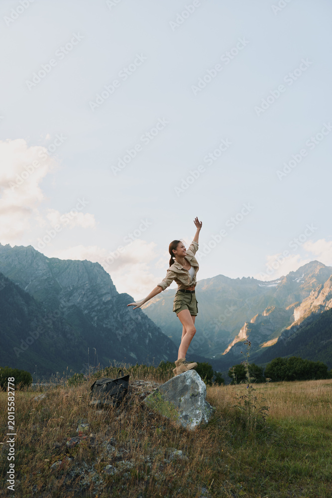 Fototapeta premium Young woman balances on a rock in a mountain meadow, enjoying fresh air and freedom.