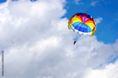 Paragliding using a parachute on background of blue cloudy sky.