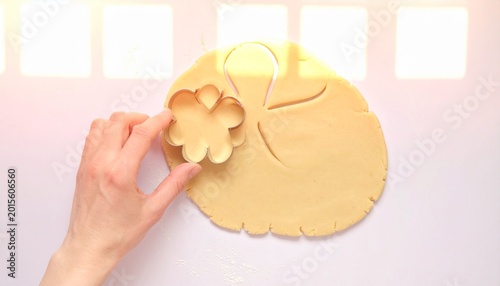 Hand pressing flower-shaped cookie cutter into dough on light surface