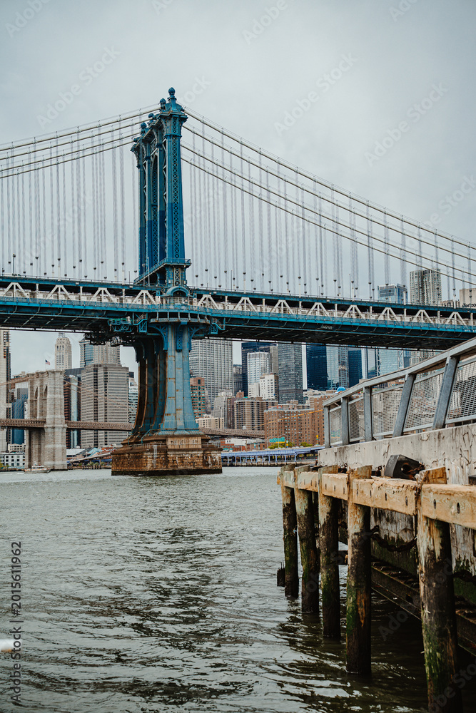 Fototapeta premium View of Manhattan Bridge tower from East River wooden pier. Steel suspension tower of Manhattan Bridge seen from a weathered wooden dock on the riverfront.