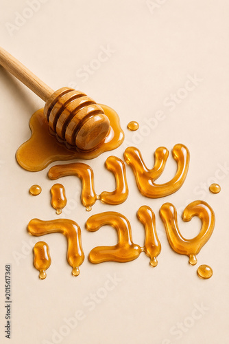 Minimalist Rosh Hashanah concept featuring glossy honey typography in Hebrew spelling “Shana Tova” on a light neutral background. Creative food typography with realistic honey texture