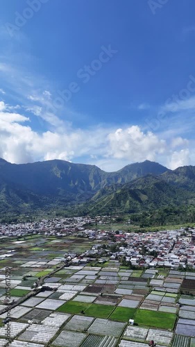 Lush Green Farmland and Rural Village Nestled Amidst Majestic Mountains under a Clear Blue Sky