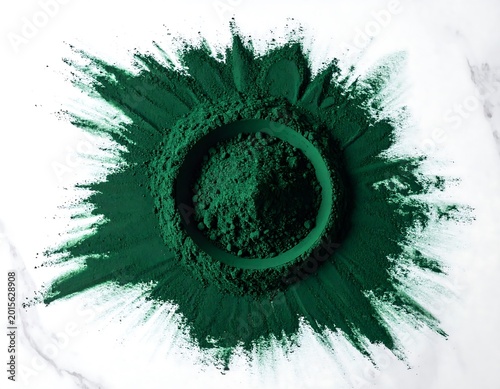 Symmetrical spirulina powder blast on white marble surface, artistic green pigment burst for health and beauty.