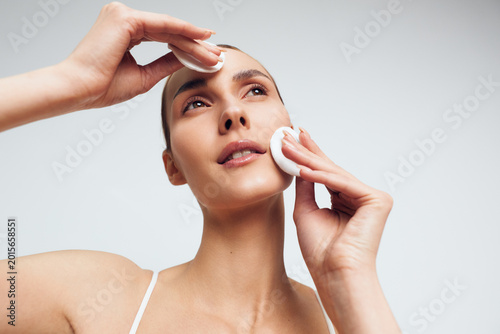 Obraz na plátně Clear portrait of a woman performing a facial cleansing routine, removing makeup with cotton pads, close up on the face, soft lighting, calm skincare moment, studio shot