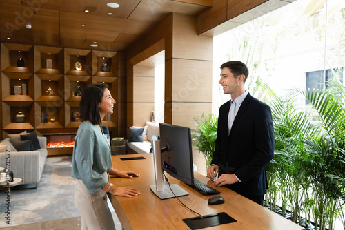 Fotografie Female guest standing at hotel reception desk speaking with male receptionist during check-in