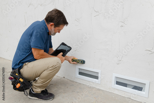 An environmental home inspector is viewed close-up at work, using an electronic moisture meter to detect signs of damp and rot in structural elements.