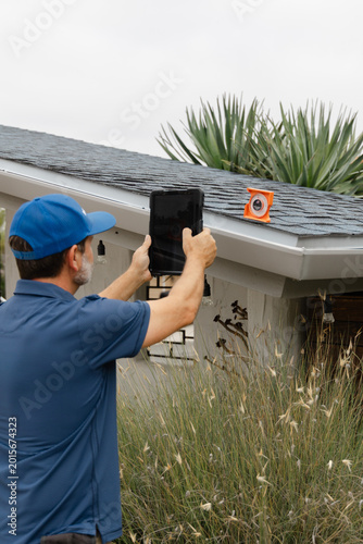 A home inspector is using a pitch and slope locator to measure the roof pitch of a residential home. Roof inspection.