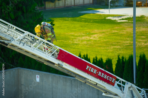 Photos Firefighter in yellow turnout gear and yellow helmet with SCBA climbing aerial laddder with grass field in background