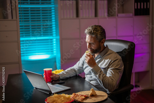 Freelancer eat pizza late at night. Night office with laptop and snack. Night office relaxation. Night job. Businessman eat snack while working on laptop. Busy employee office work during late night