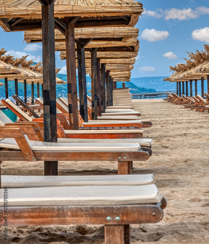 Photos Rows of Wooden Sunbeds and Thatched Umbrellas on a Sandy Beach distant hills in the background