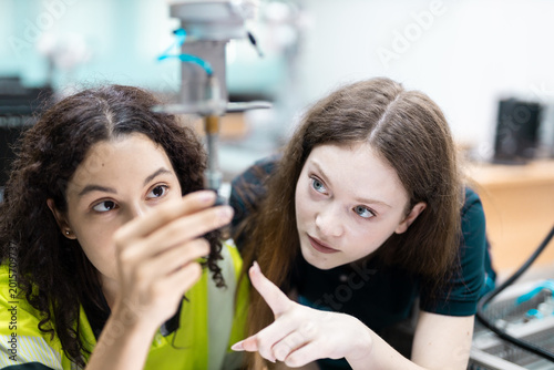 Engaged young woman student engineer in teamwork, learning about robot technology with robotic arm. Future education for industry automation and modern programming for machinery
