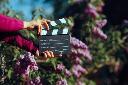 Hands Holding Cinema Clapperboard Outdoors In Front Of Blooming Lilacs. Director shooting video production outdoors in springtime blooming setting 