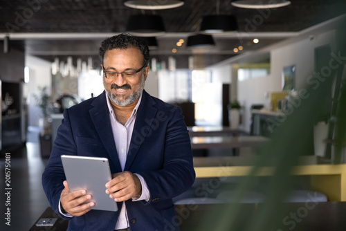 Foto Middle-age businessman holding digital tablet standing in coworking office, revi