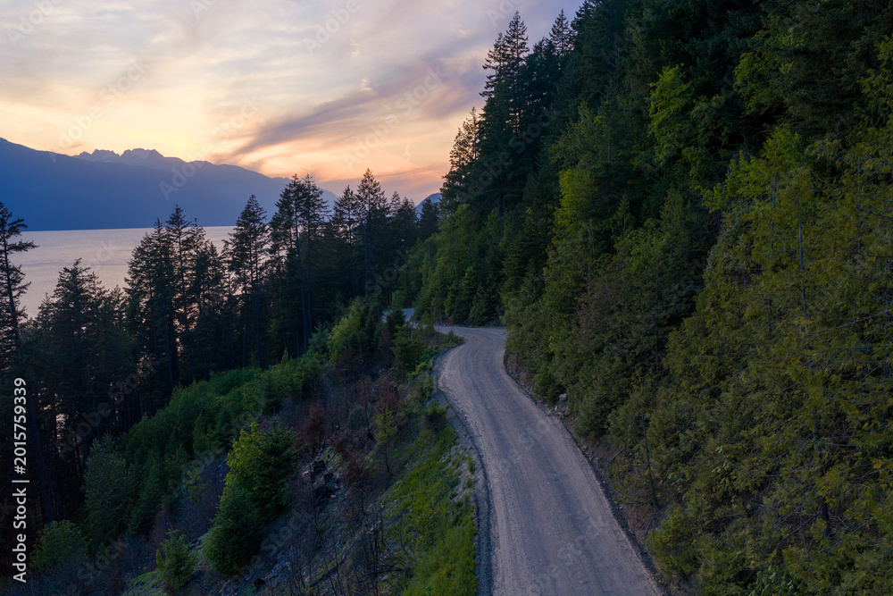 Obraz premium Winding Dirt Road Along Forested Hills Overlooking Lake at Sunset in British Columbia Canada