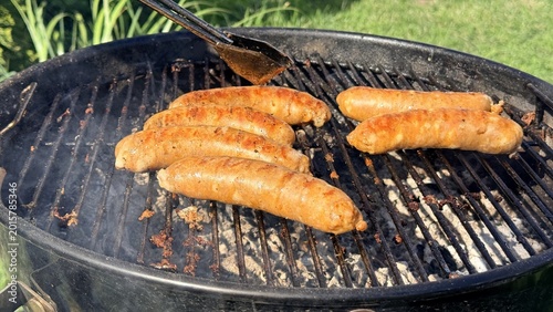 Fotografie Grilled sausages cooking on outdoor barbecue grill, summer backyard cookout scen