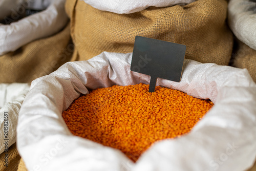 Close-up photo of a white sack containing red lentils and a black wooden sign.