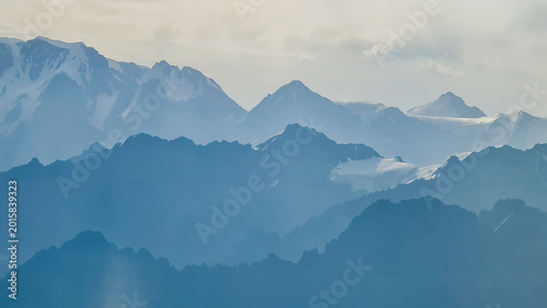 Artistic telephoto shot of distant mountain ridges creating blue layers of silhouettes under a soft sky. Minimalist mountain landscape.