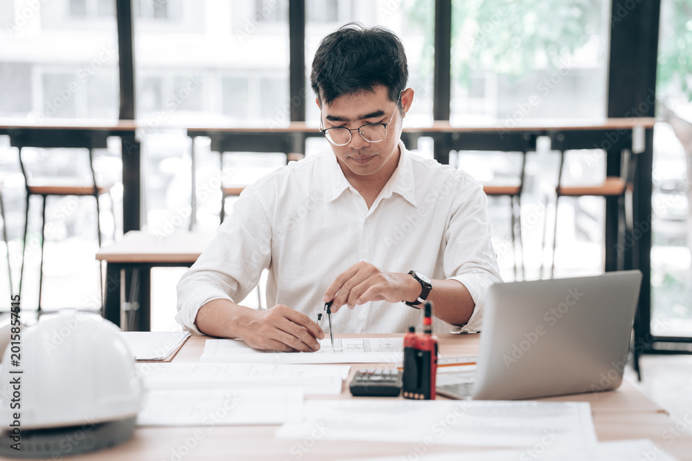 Fototapeta premium Young male architect or engineer reviewing blueprints at desk in modern office
