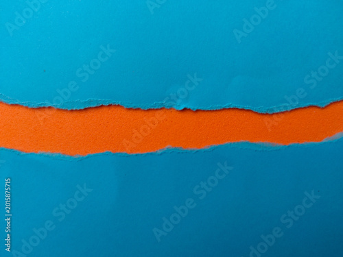 A horizontal strip of textured orange foam is revealed through a jagged tear in blue paper