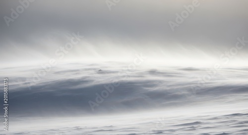 Intense blizzard sweeping across a desolate landscape, featuring heavy blowing snow, frigid temperatures, and dangerously low visibility under a gray sky, extreme, texture, severe