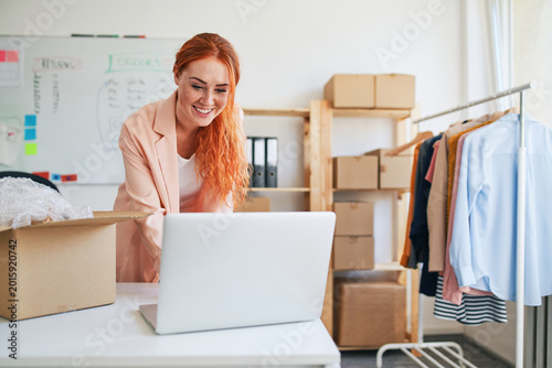 Young woman managing online clothing shop at laptop in warehouse
