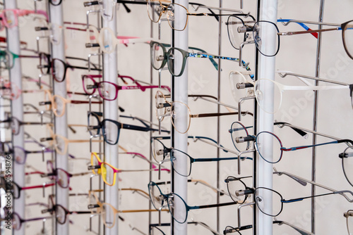 Collection of eyeglasses frames hanging on white display rack in optical shop interior with variety of styles and colors for vision care retail