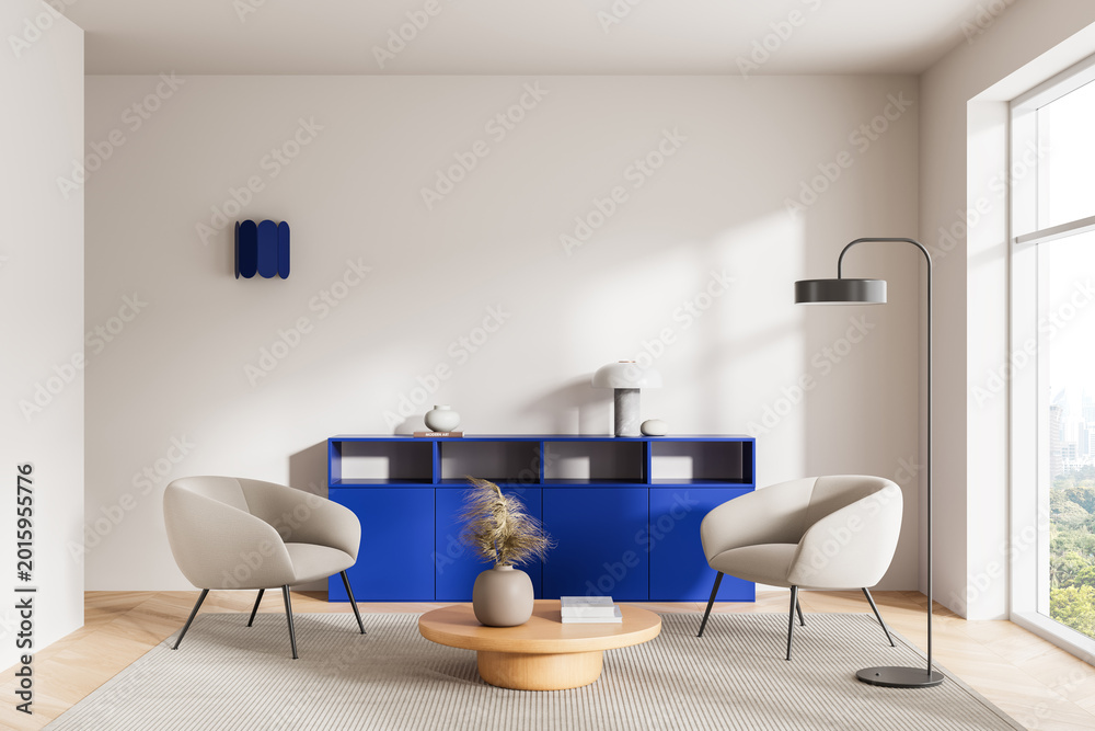 Fototapeta premium Modern interior lounge with beige chairs, bold blue cabinet, rounded wooden table, floor lamp and soft daylight forming a calm contemporary design scene. 3D Rendering