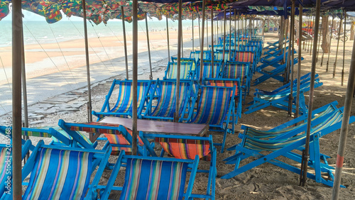 Foto Colorful beach chairs lined up under shaded umbrellas along a tropical seaside in Thailand