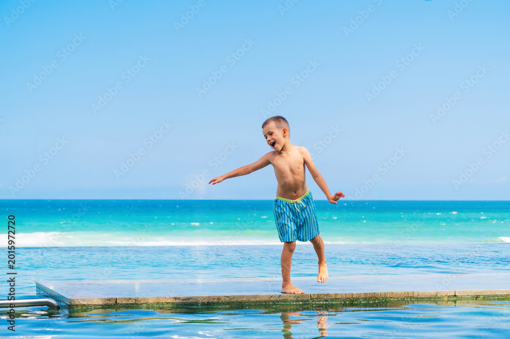 Fototapeta premium happy child playing in infinity pool by tropical ocean