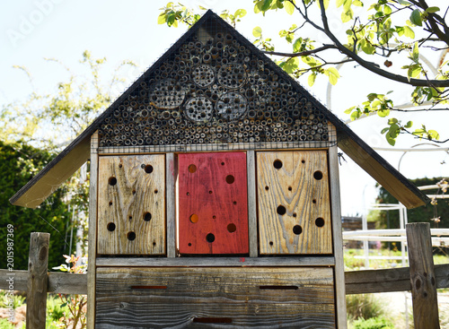 A detailed view of a wooden insect hotel filled with natural materials and nesting holes. The structure supports biodiversity and offers shelter for beneficial insects in a garden setting.