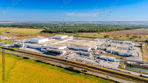 Panoramic aerial view of large industrial plant in rural area. Wide landscape showing a massive manufacturing complex with utility structures and roads under a clear blue sky.