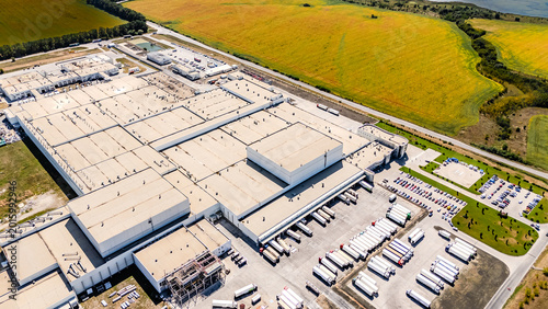 Top down aerial view of distribution center loading docks. Logistics facility showing rows of trucks parked at loading bays near yellow fields.